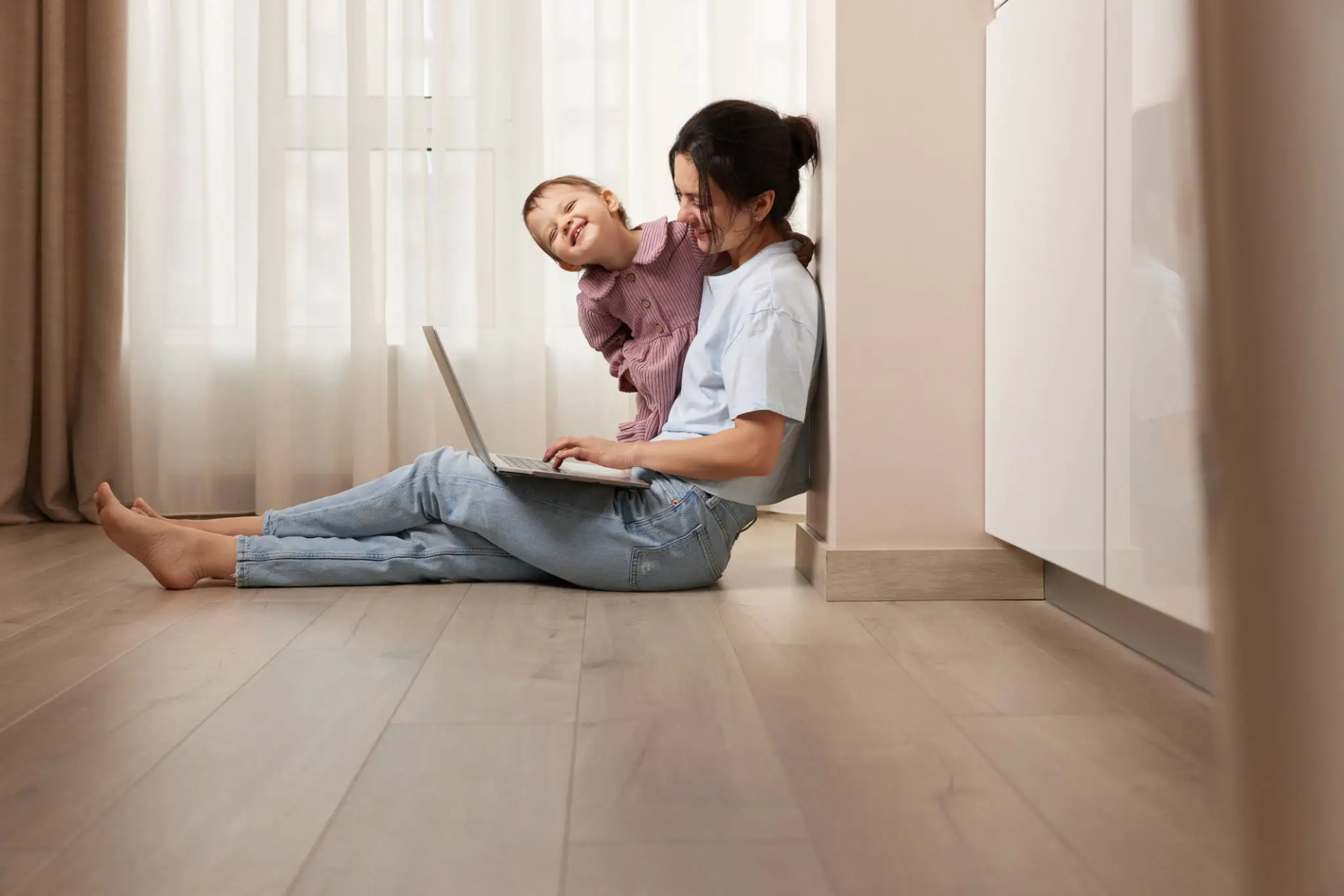 Woman working on laptop, child playing nearby.